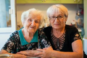 older woman sits with senior daughter with glasses